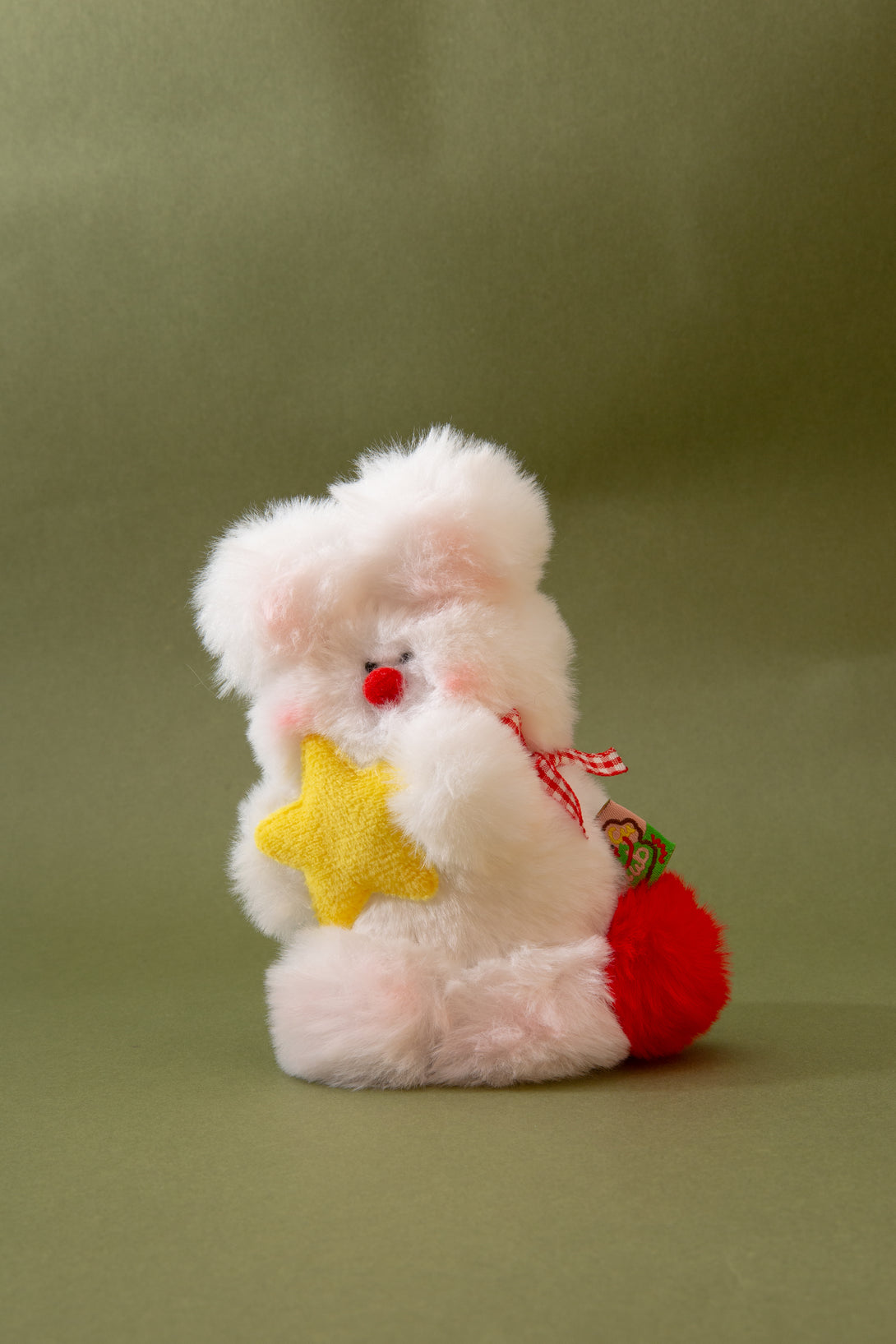 Plush key chain resembling a rabbit holding a yellow star and red bag on a green background