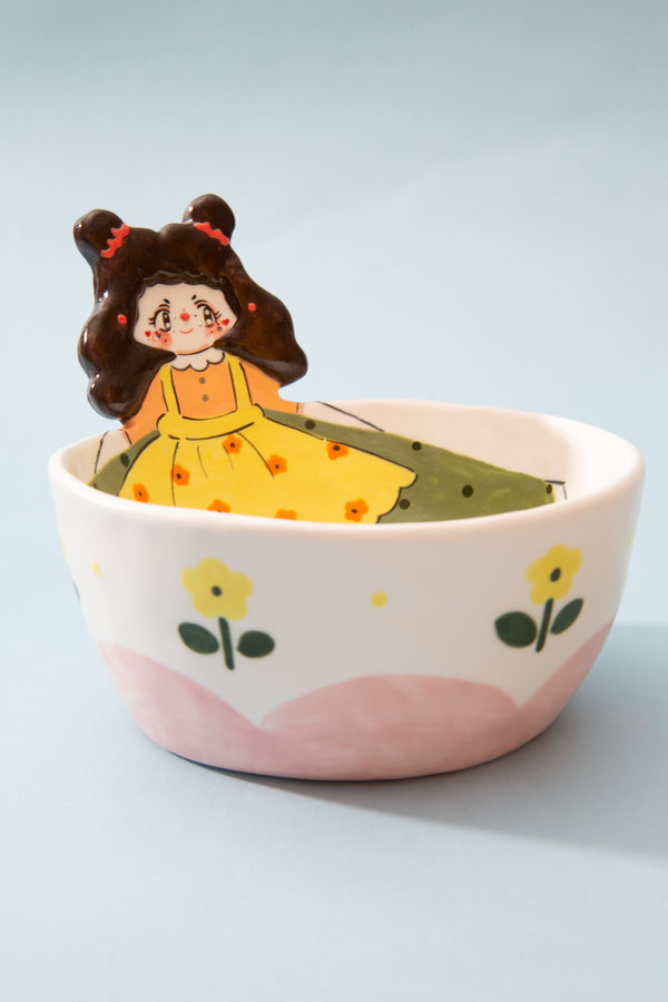 Ceramic bowl with a decorative design of a girl in a yellow dress and flowers on a light blue background.