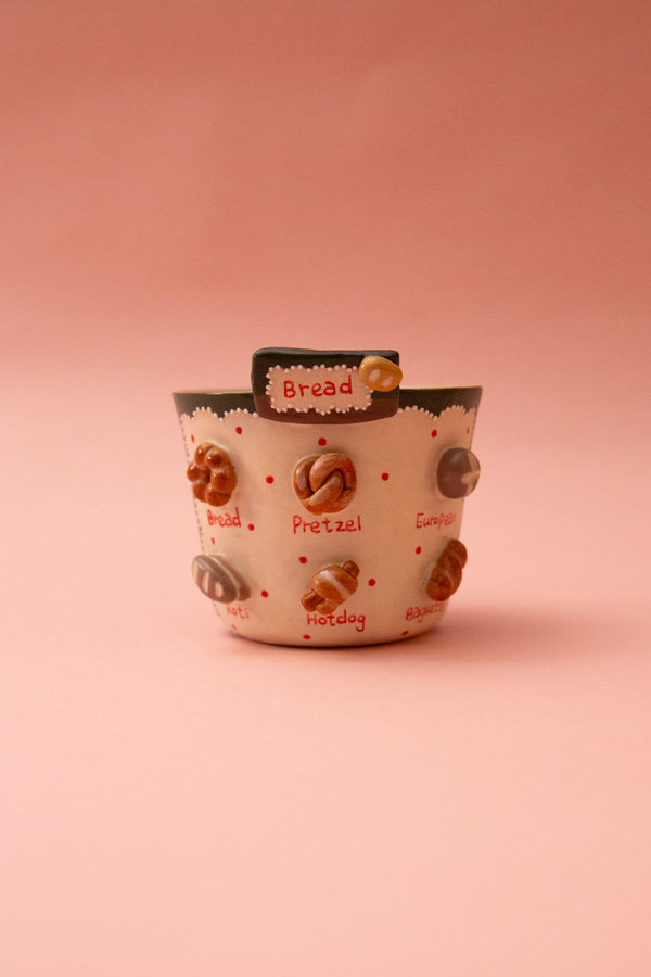 Ceramic mug with bread-themed design on a pink background