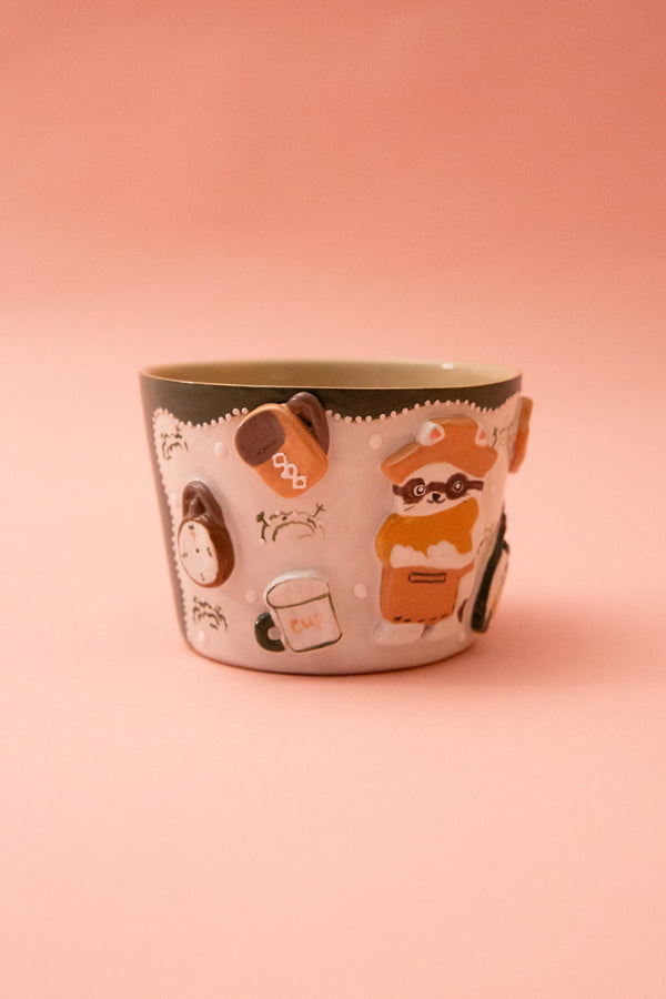 Ceramic mug with cartoon raccoon design on a pink background