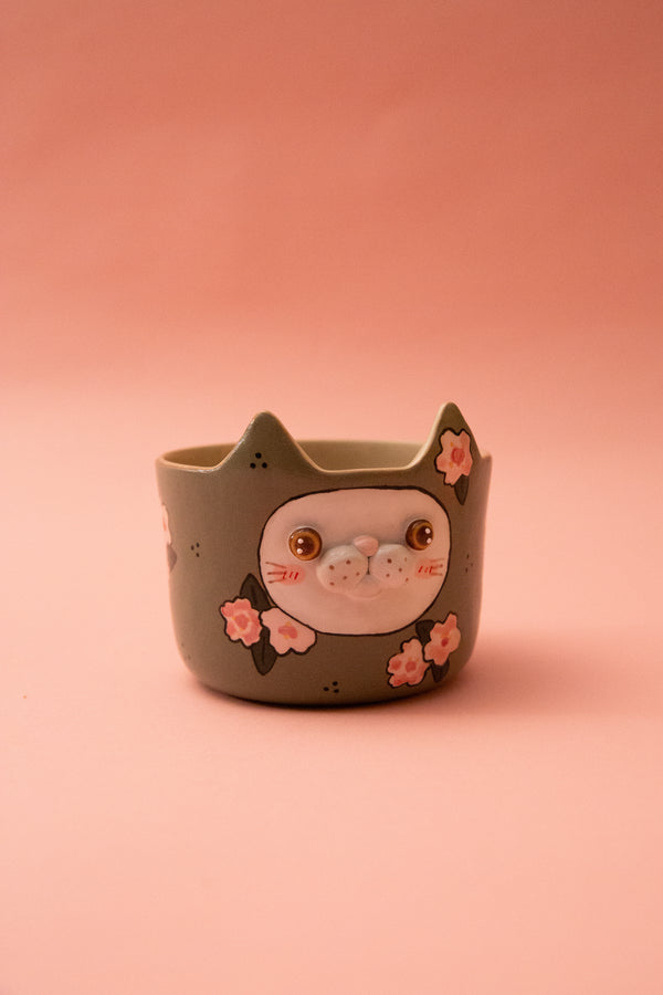 Ceramic cat-shaped mug with face and flowers on a pink background