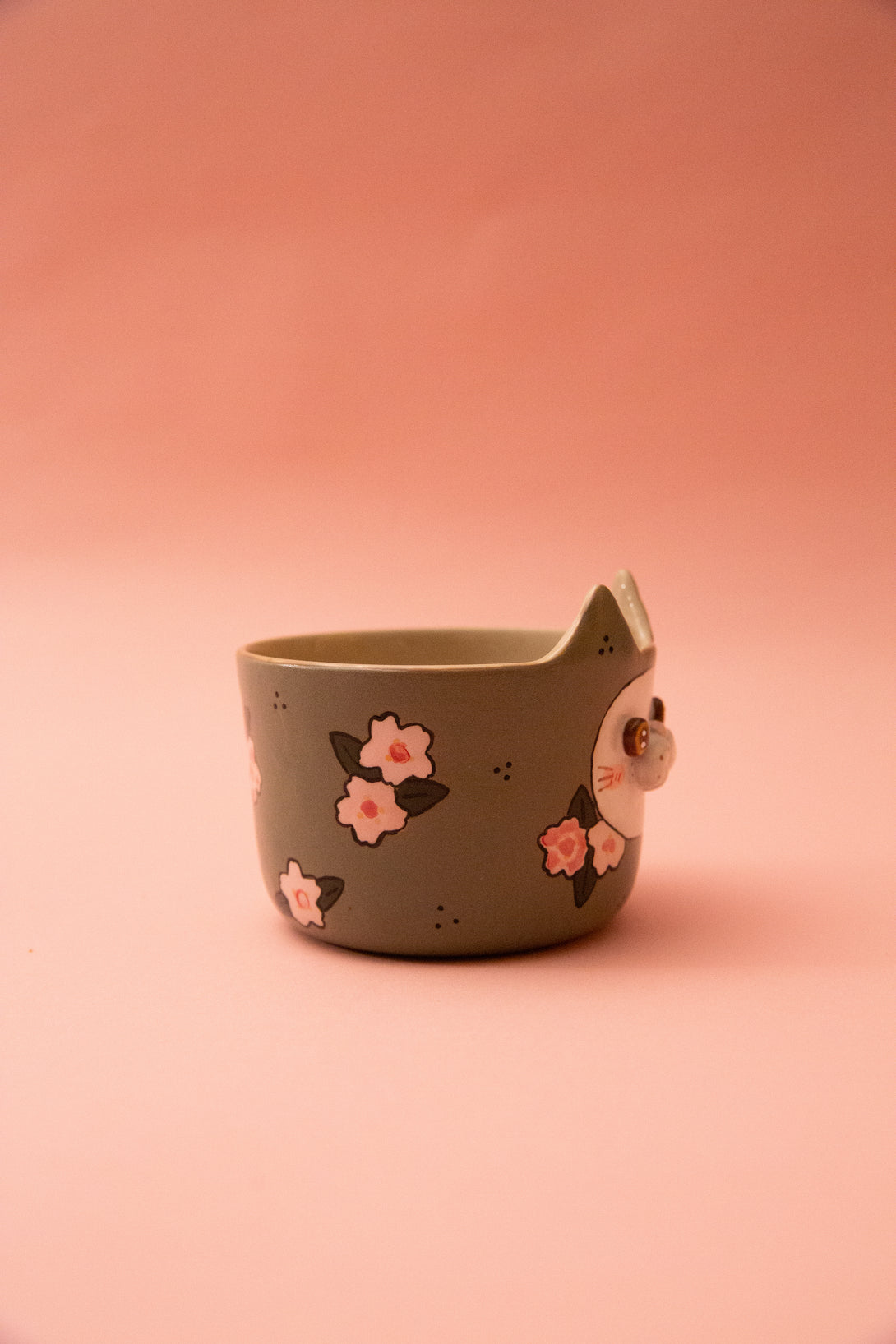 Ceramic mug with a cat design and floral patterns on a pink background