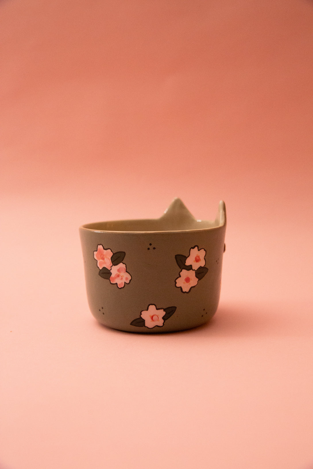Green ceramic cup with pink floral designs on a pink background
