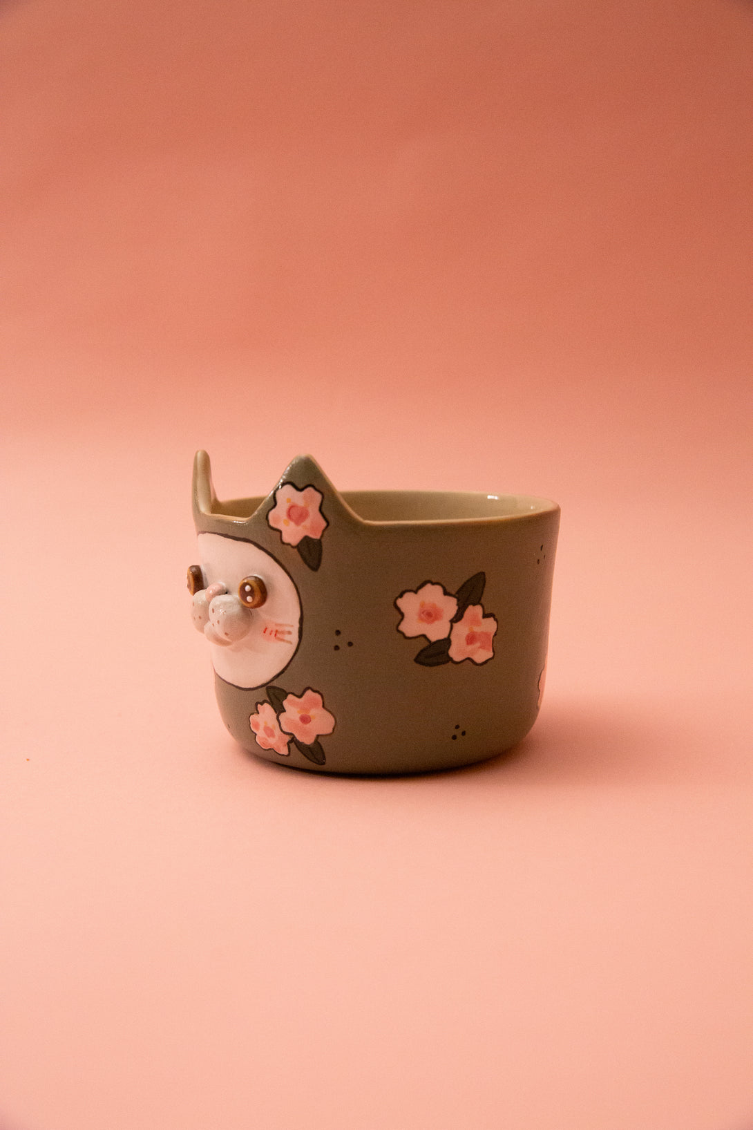 cup with a cat design and floral elements on a pink background