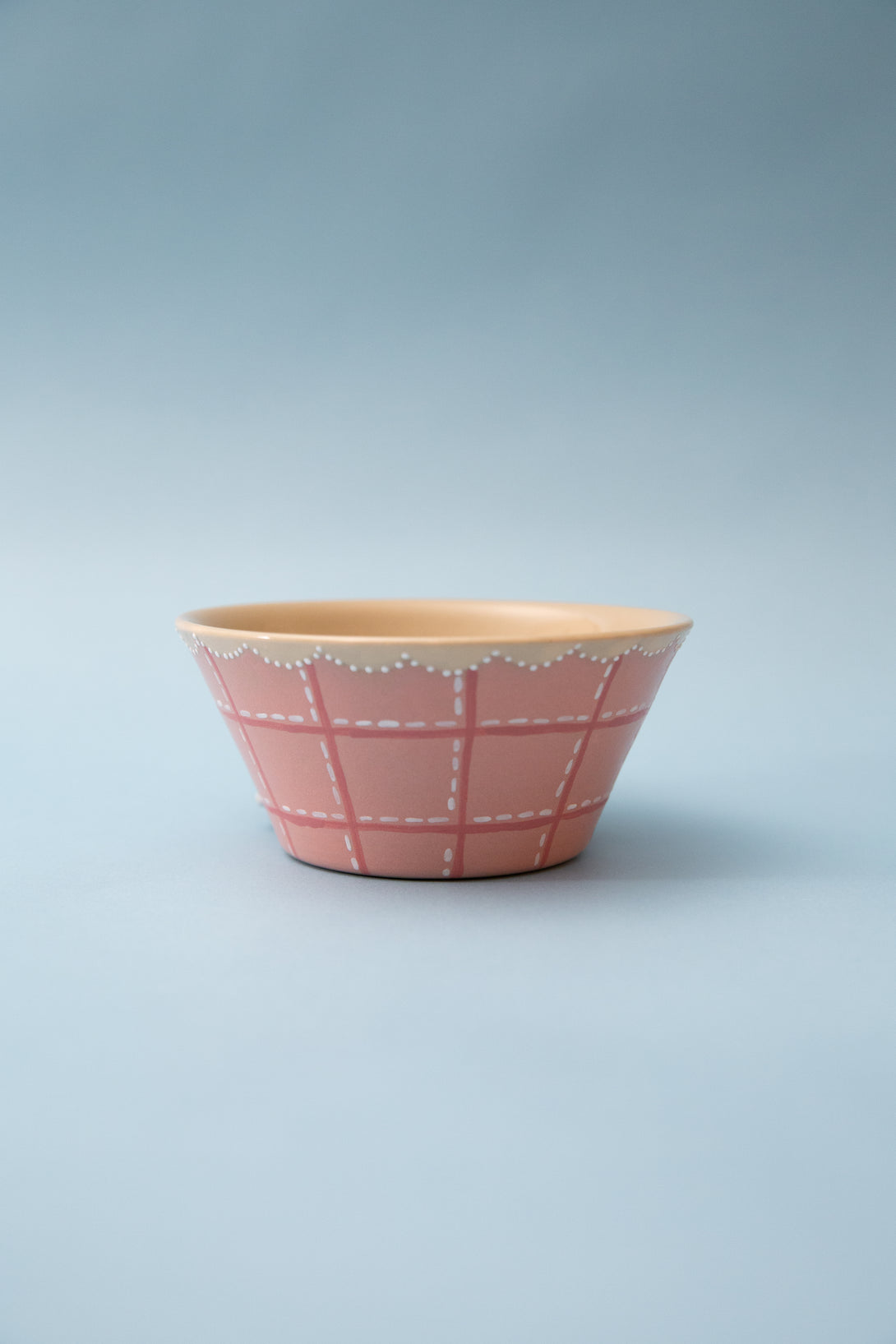 Pink ceramic bowl with white checkered pattern on a light gray background