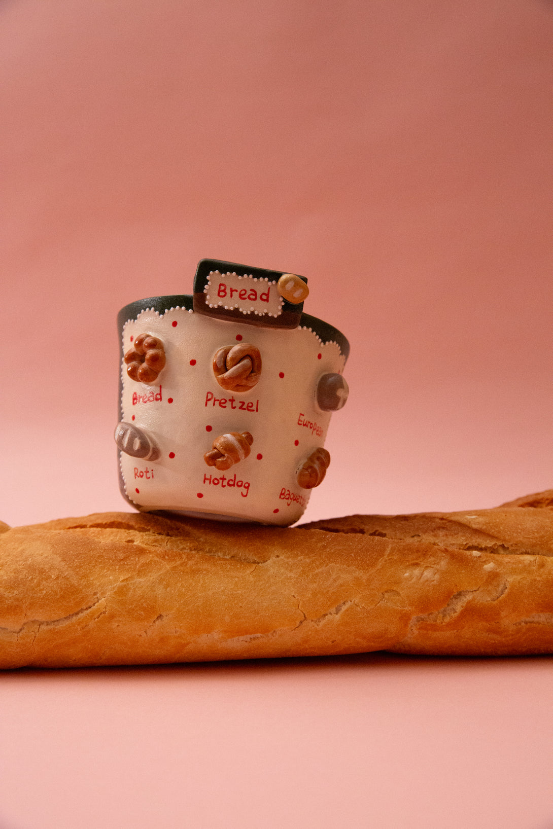 ceramic mug with bread-themed design and a bread loaf on a pink background
