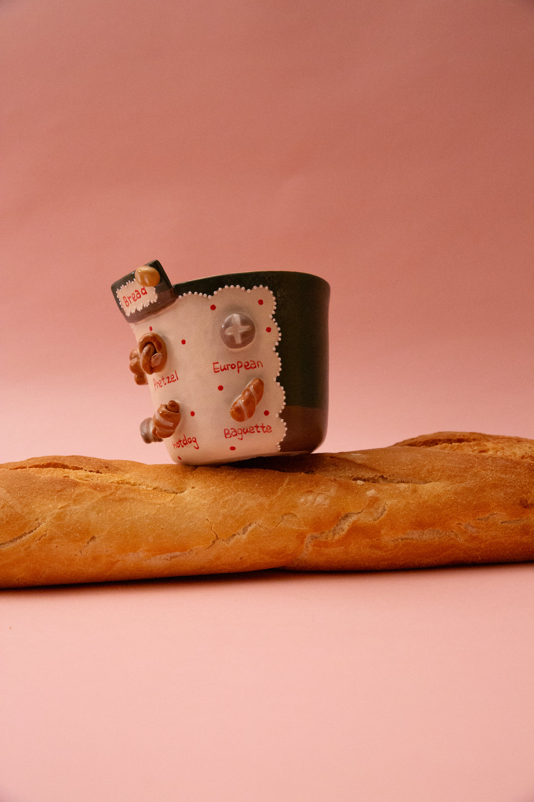  handmade mug with a bread-themed design on top of a long baguette against a pink background
